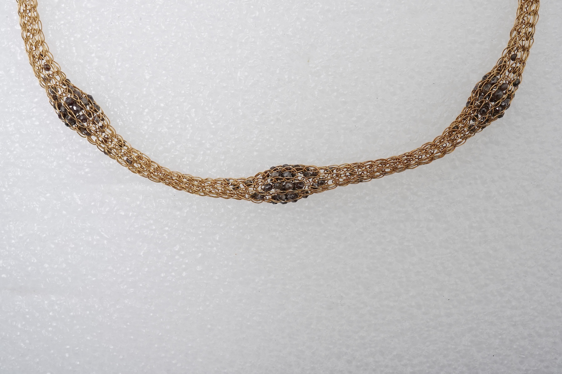 An 18ct gold and diamond necklace, composed of a woven tube of 18ct gold wire links, three sections threaded with brown diamond beads, length approximately 45cm, British hallmarks, sponsor's mark TJH, gross weight approx